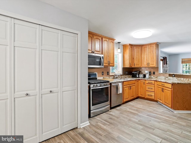 kitchen with pendant lighting, light stone counters, appliances with stainless steel finishes, a peninsula, and light wood-style floors