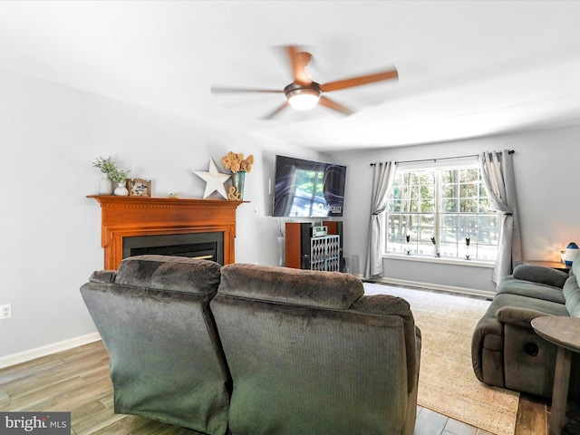 living room with a fireplace, wood finished floors, baseboards, and a ceiling fan