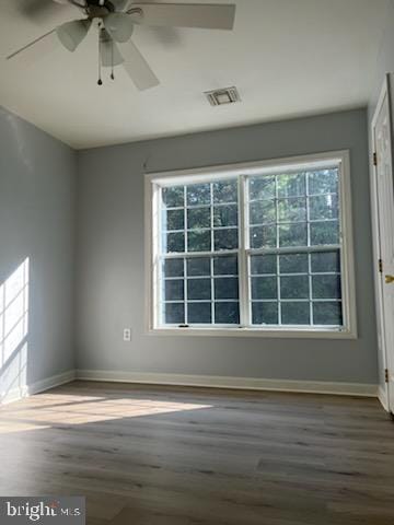 empty room with a ceiling fan, wood finished floors, visible vents, and baseboards