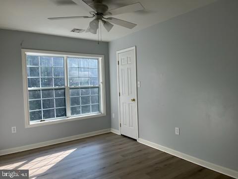 empty room with visible vents, ceiling fan, dark wood-type flooring, and baseboards