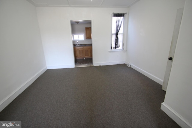 empty room featuring baseboards and dark colored carpet