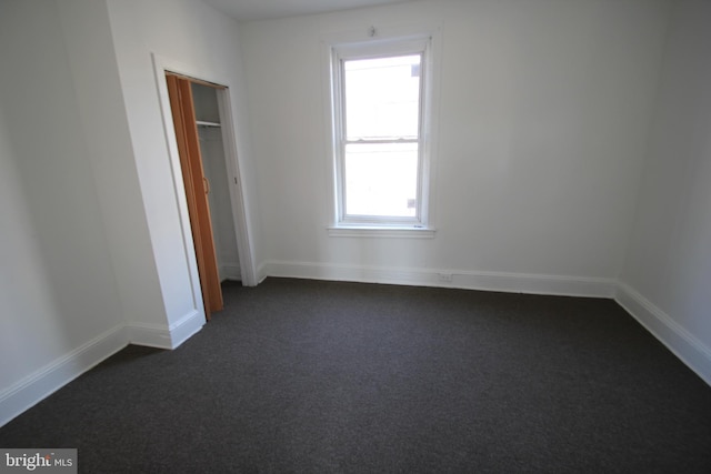 unfurnished bedroom featuring a closet, baseboards, and dark colored carpet