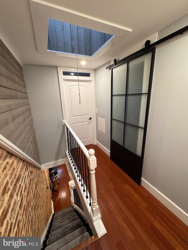 staircase with baseboards, a barn door, and wood finished floors