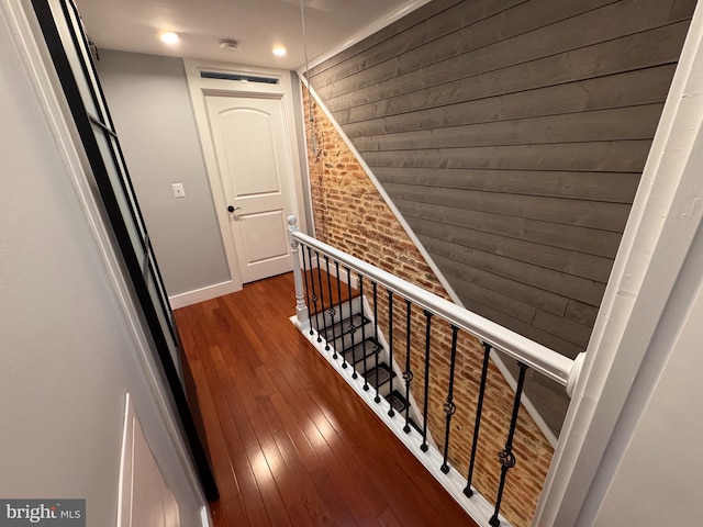 hallway featuring an upstairs landing, dark wood-style floors, brick wall, and baseboards