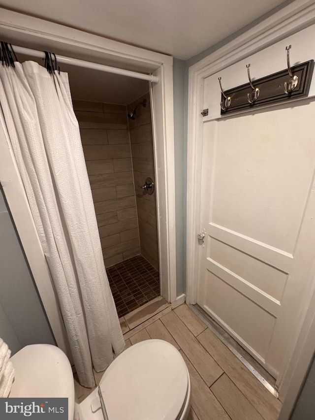 full bath with a stall shower, toilet, and wood finish floors