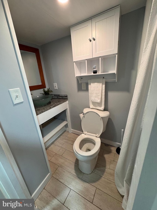 bathroom featuring a sink, toilet, baseboards, and wood tiled floor