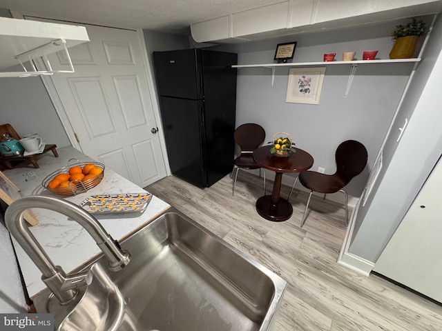 kitchen with a sink, light wood-type flooring, open shelves, and freestanding refrigerator