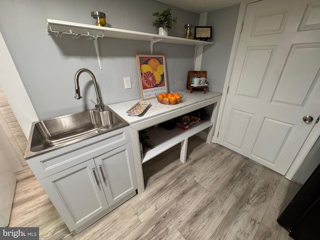 kitchen with light wood finished floors, open shelves, light countertops, white cabinets, and a sink