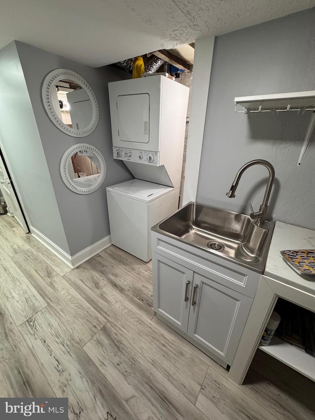 washroom featuring a sink, light wood-style floors, stacked washer / dryer, baseboards, and laundry area