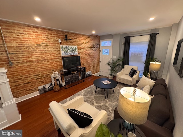 living room featuring recessed lighting, wood finished floors, baseboards, and brick wall