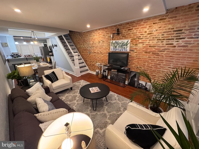 living area with stairs, recessed lighting, wood finished floors, and brick wall