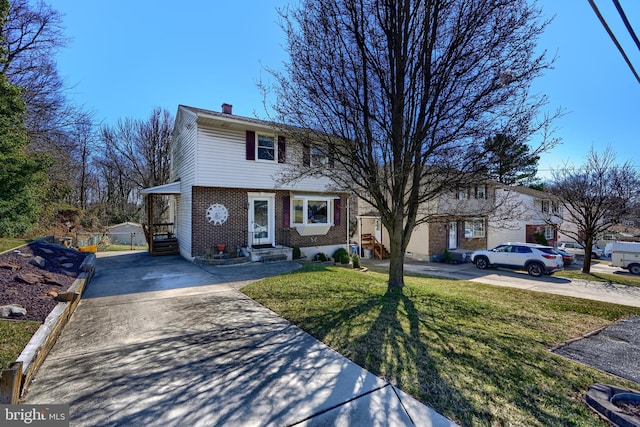 view of front of property featuring driveway, a front yard, brick siding, and a chimney