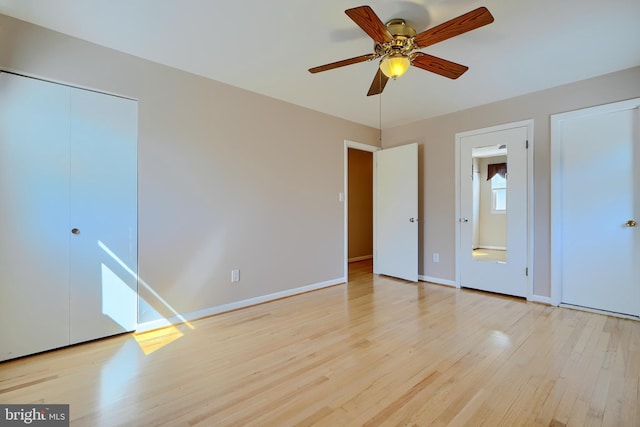 unfurnished bedroom featuring a ceiling fan, wood finished floors, baseboards, and multiple closets