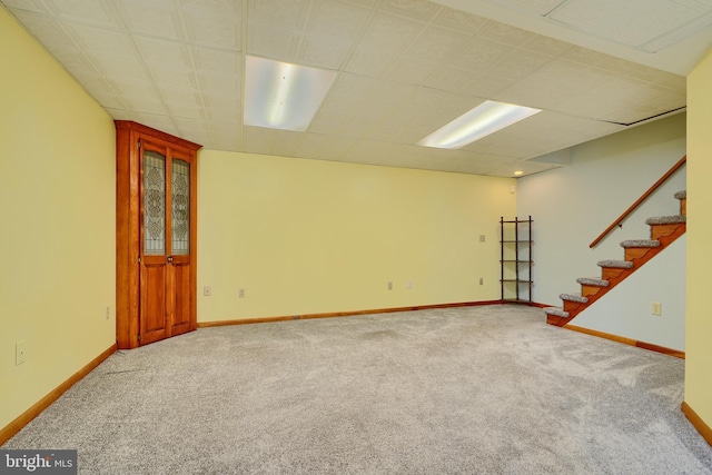 carpeted empty room featuring stairway and baseboards