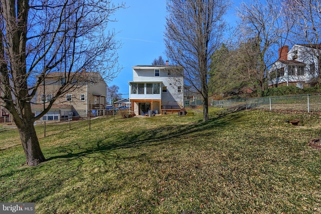 rear view of property featuring a lawn, a fenced backyard, a sunroom, and a chimney