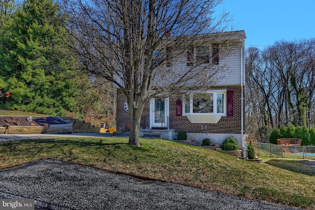 colonial-style house featuring brick siding, a front yard, and fence