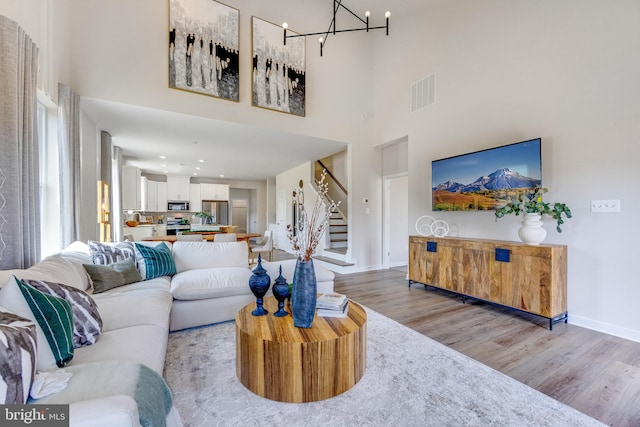 living area with light wood-type flooring, visible vents, stairway, baseboards, and a chandelier