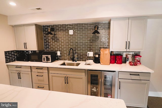 kitchen with visible vents, backsplash, beverage cooler, light countertops, and a sink