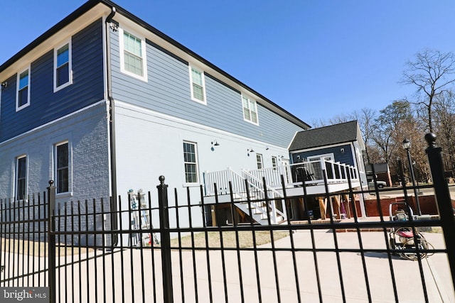 view of side of home featuring stairs, fence, brick siding, and a wooden deck