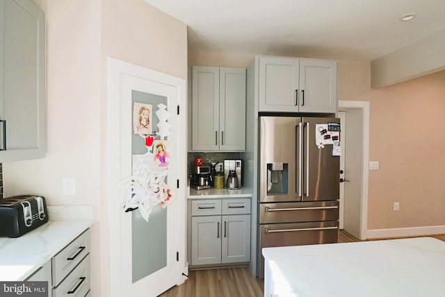 kitchen featuring tasteful backsplash, baseboards, light stone counters, light wood-style flooring, and stainless steel fridge