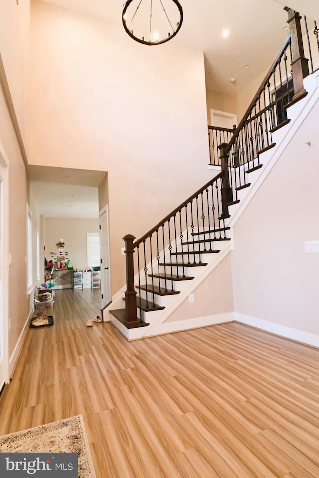 entryway with wood finished floors, an inviting chandelier, baseboards, a towering ceiling, and stairs