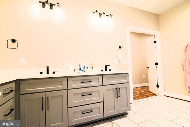 bathroom featuring double vanity, baseboards, marble finish floor, and a sink