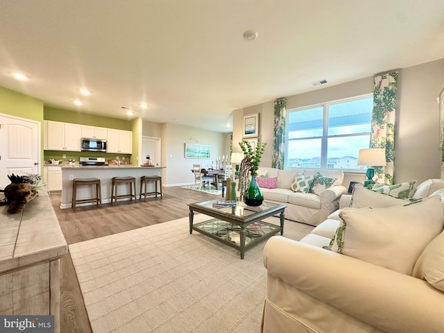 living area featuring visible vents, recessed lighting, baseboards, and light wood-style floors