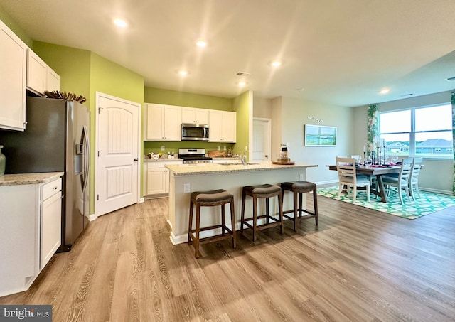 kitchen with a center island with sink, light wood finished floors, stainless steel appliances, white cabinetry, and a kitchen breakfast bar