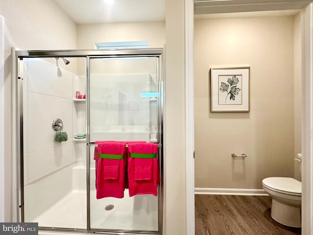 bathroom with a stall shower, baseboards, toilet, and wood finished floors