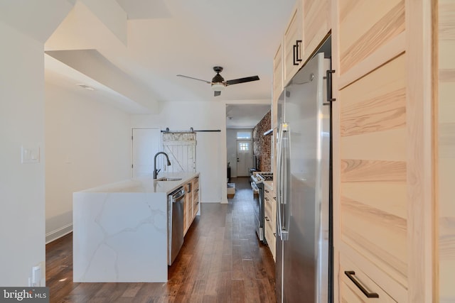 kitchen featuring a barn door, light stone counters, appliances with stainless steel finishes, a ceiling fan, and dark wood-style flooring