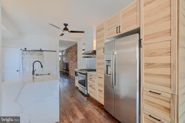 kitchen with a barn door, dark wood-style floors, stainless steel appliances, a ceiling fan, and a sink