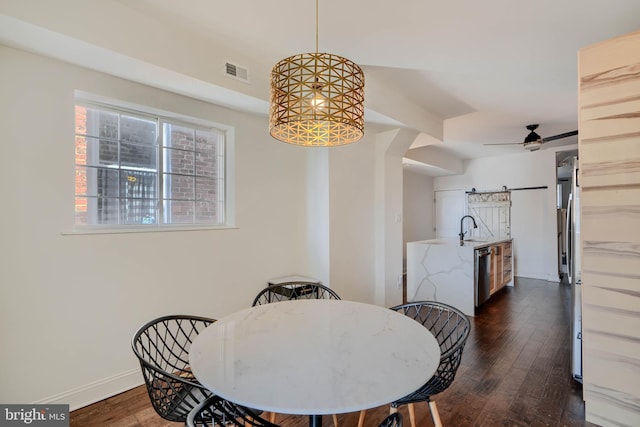 dining space featuring a barn door, visible vents, dark wood-style flooring, and ceiling fan with notable chandelier