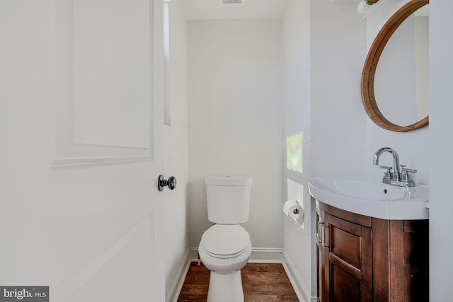 half bath with visible vents, baseboards, toilet, wood finished floors, and vanity