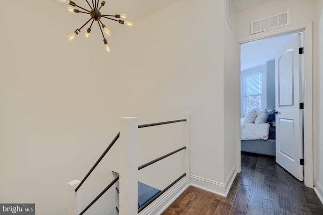 corridor with baseboards, visible vents, dark wood-type flooring, an upstairs landing, and a chandelier