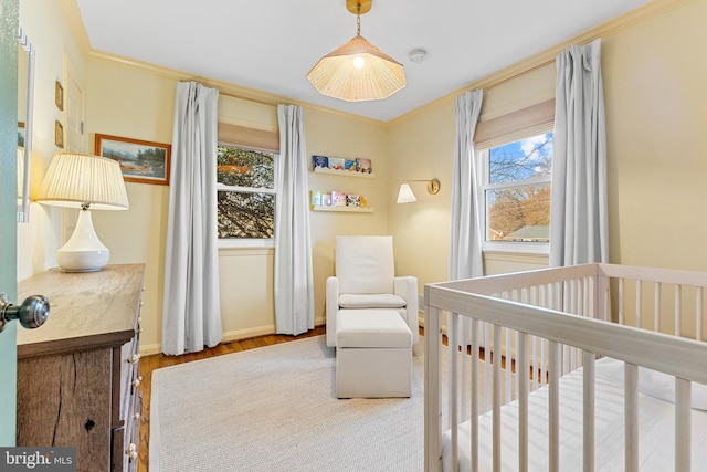 bedroom with baseboards, a nursery area, wood finished floors, and ornamental molding