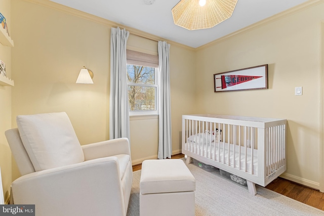 bedroom with a nursery area, wood finished floors, baseboards, and ornamental molding