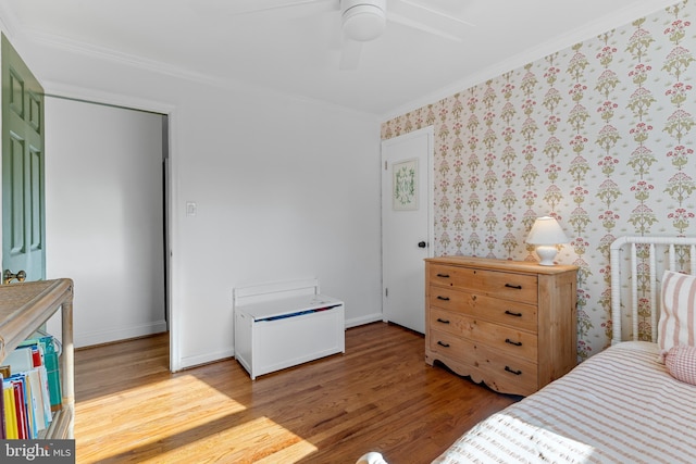 bedroom with wallpapered walls, crown molding, baseboards, and wood finished floors