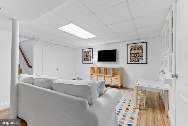 living room featuring baseboards, a paneled ceiling, light wood-style flooring, and stairs