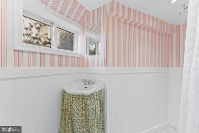 bathroom with a wainscoted wall, wallpapered walls, and a sink