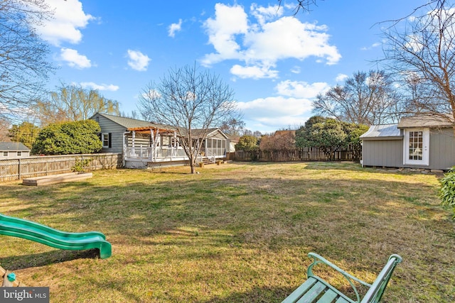 view of yard featuring a playground, a storage shed, a fenced backyard, a deck, and an outbuilding