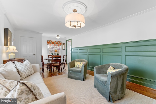 living area featuring light wood finished floors, a decorative wall, wainscoting, and crown molding