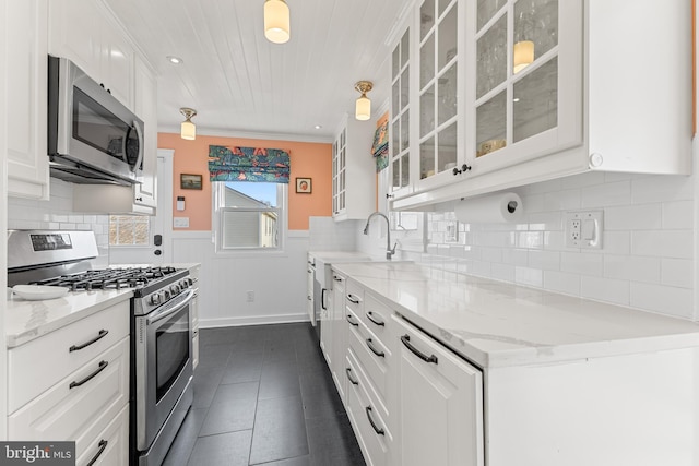 kitchen featuring white cabinetry, light stone countertops, a wainscoted wall, and stainless steel appliances