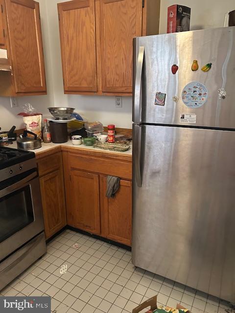 kitchen featuring brown cabinetry, light tile patterned floors, stainless steel appliances, and under cabinet range hood