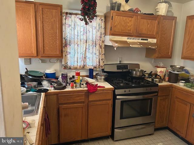 kitchen with brown cabinets, under cabinet range hood, a sink, gas stove, and tile counters