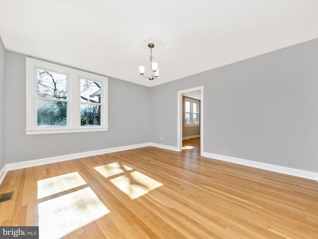 spare room with visible vents, baseboards, an inviting chandelier, and wood finished floors