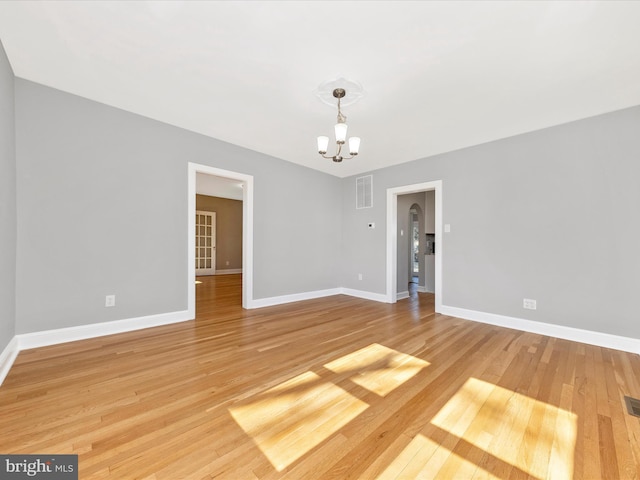 spare room with an inviting chandelier, baseboards, visible vents, and light wood finished floors