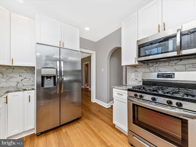 kitchen featuring arched walkways, white cabinets, appliances with stainless steel finishes, and light stone countertops