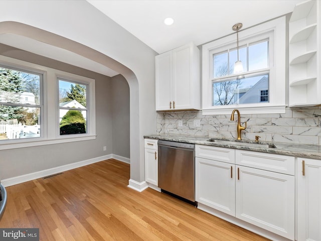 kitchen with dishwasher, light stone counters, arched walkways, white cabinetry, and a sink