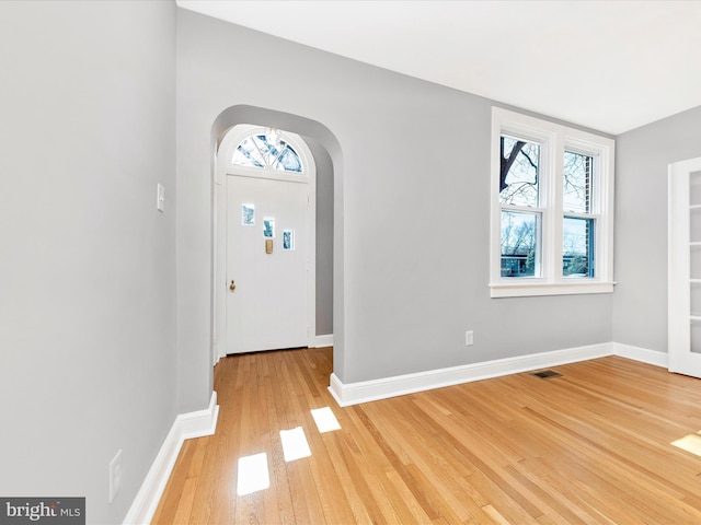 foyer with light wood finished floors, baseboards, arched walkways, and a wealth of natural light