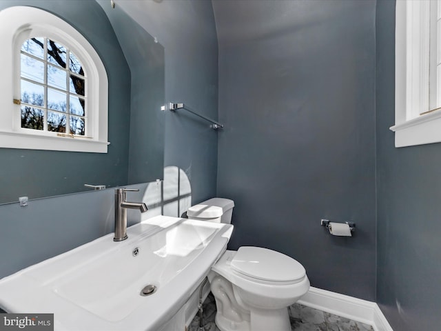 bathroom with marble finish floor, toilet, baseboards, and a sink